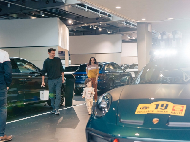 Familie-lachend-neben-dem-Porsche-Dakar-in-dunkel-gruen