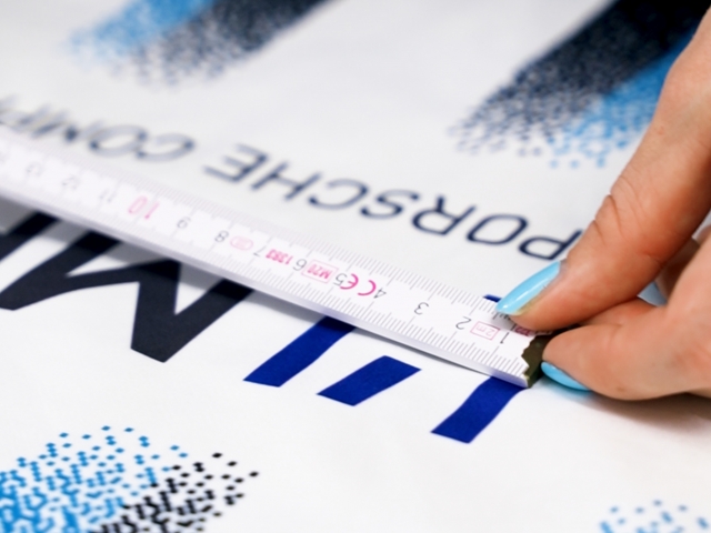 Detailfoto-von-weiblicher-Hand-mit-hellblauen-Fingernaegel-welche-Maßstab-an-dunkelblaues-Logo-haelt-stuttgarter-kickers-trikot