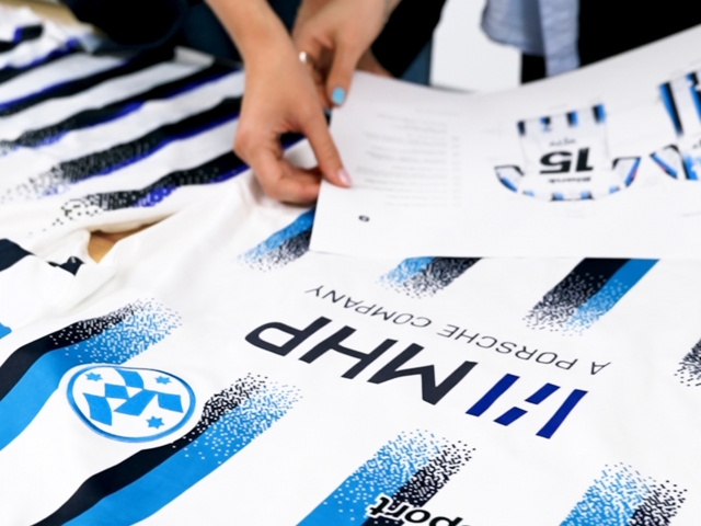 Detailfoto-von-weiblicher-Hand-mit-hellblauen-Fingernaegel-welche-Maßstab-an-dunkelblaues-Logo-haelt-stuttgarter-kickers-trikot