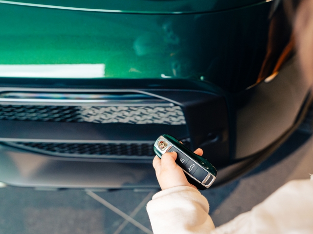 Kind-drueckt-Auto-Fernbedienung-Porsche-Dakar-dunkel-gruen-im-Hintergrund