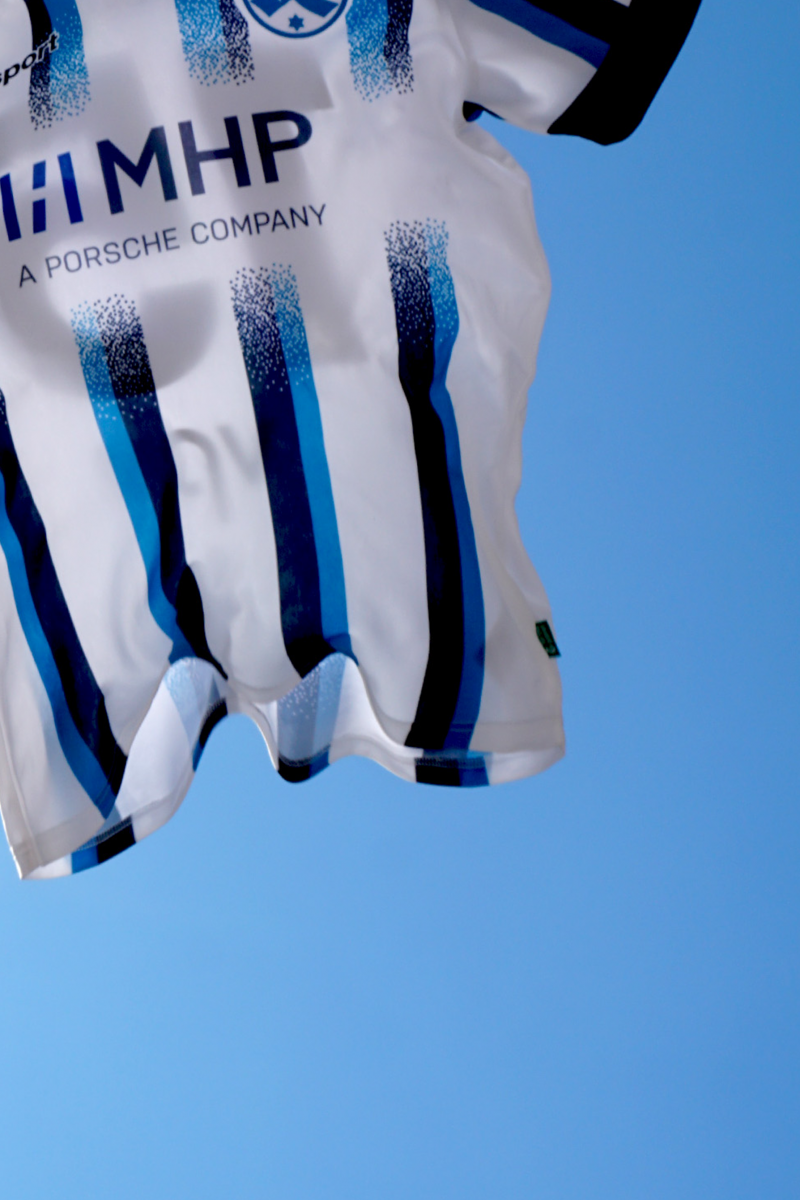 Blau-weiß-gestreiftes-Trikot-mit-mhp-Logo-und-Stuttgarter-Kickers-Logo-fliegt-vor-blauem-Himmel