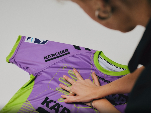 eine-ueber-die-schulter-fotografierte-frau-legt-haende-auf-trikot-und-imitiert-damit-herzdruckmassage