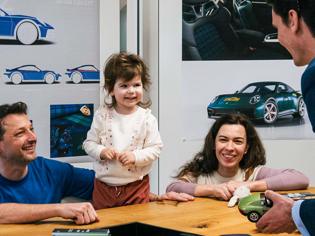 lachende-Familie-im-Besprechungsraum-Porsche-Dakar-Bilder-im-Hintergrund